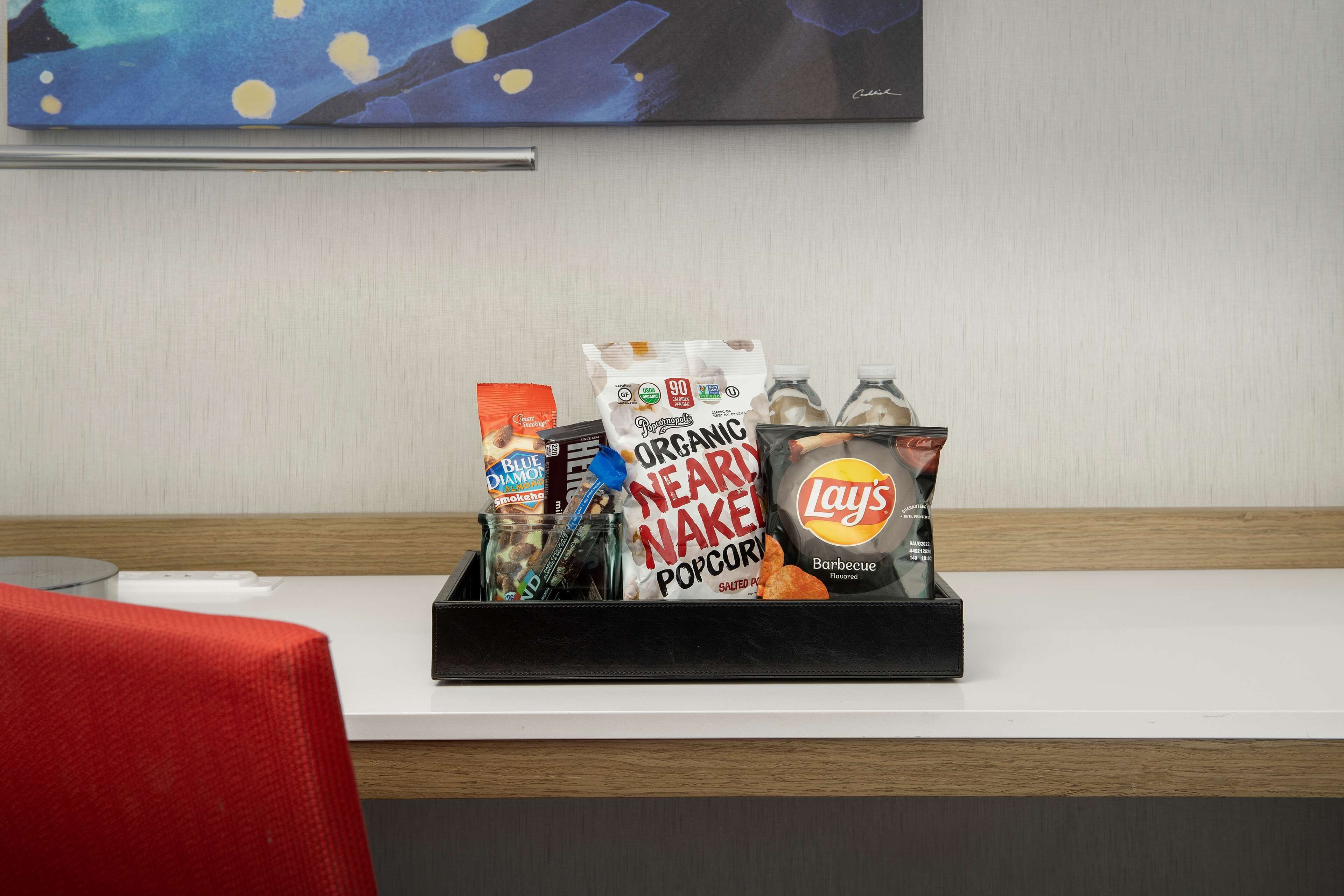 Un plat de picaruts amb diversos elements, incloent palomita de blat de moro ecològica, crispetes Lay's i altres aperitius sobre un taulell d'hotel.