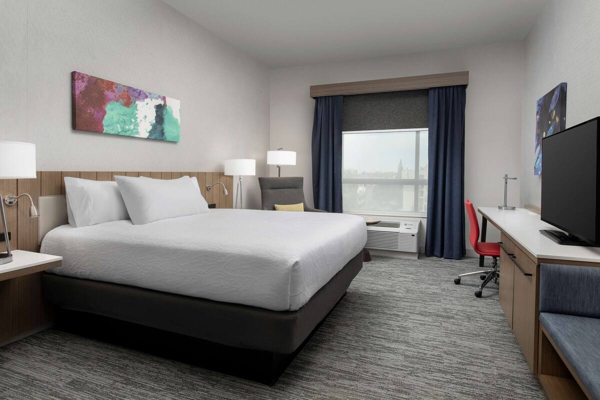 Une chambre d’hôtel avec un grand lit, un bureau, une télévision et une fenêtre avec des rideaux.