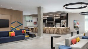 A modern hotel lobby with seating areas, a bar, and a television screen.
