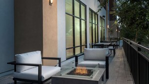 A modern outdoor seating area with a fire pit, cushioned chairs, and a railing.