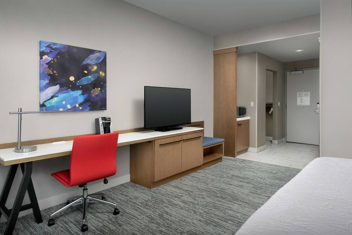 Une chambre d’hôtel équipée d’un bureau, d’une chaise, d’une télévision et d’un tableau au mur.