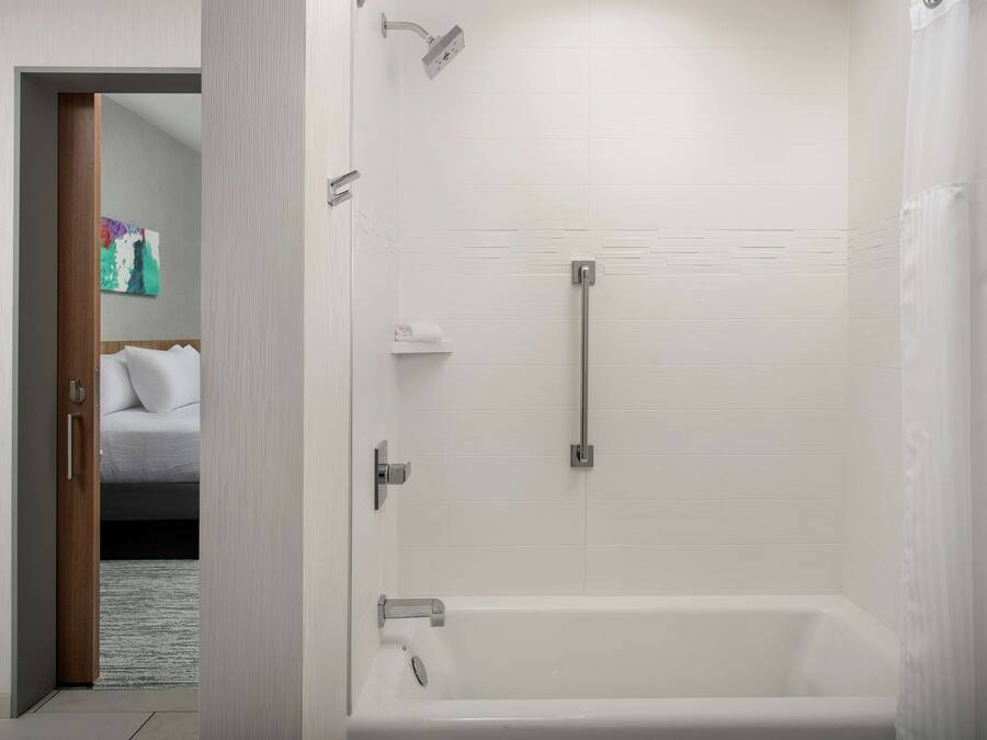 Un baño moderno con bañera, ducha y una puerta que da a un dormitorio.