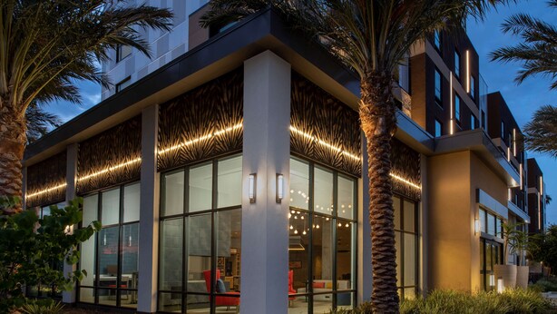 A modern hotel with large glass windows, a well-lit lobby, and a landscaped garden area.