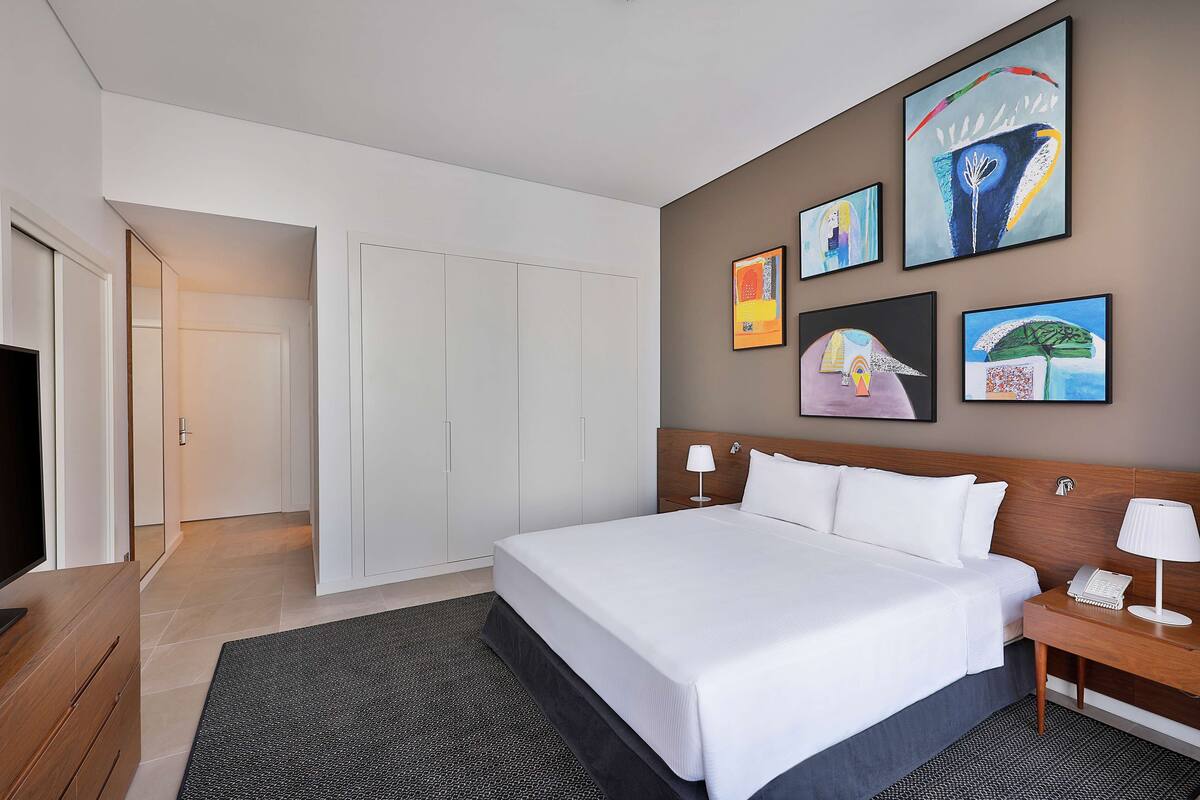 Habitació d'hotel moderna amb un llit gran, una televisió de pantalla plana, una tauleta de nit de fusta i obra d'art a les parets.