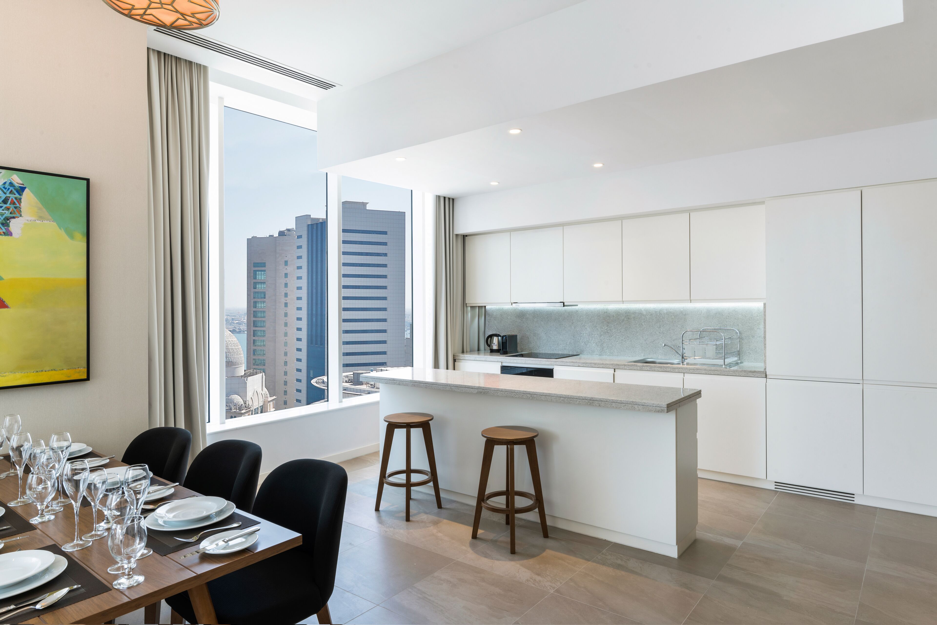 Una cocina moderna con una isla central, taburetes de bar y un comedor con una mesa dispuesta para seis personas.