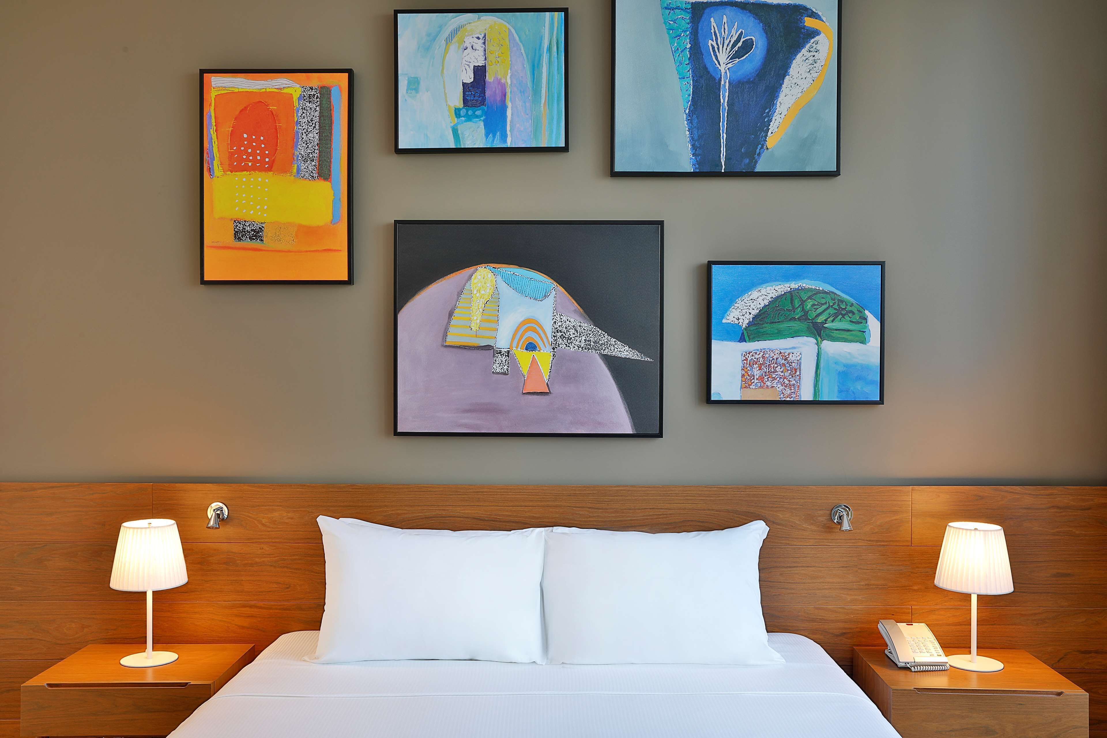 Een hotelkamer met een bed, twee nachtkastjes met lampen en vier kunstwerken in lijsten aan de muur.