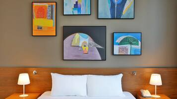 Een hotelkamer met een bed, twee nachtkastjes met lampen en vier kunstwerken in lijsten aan de muur.