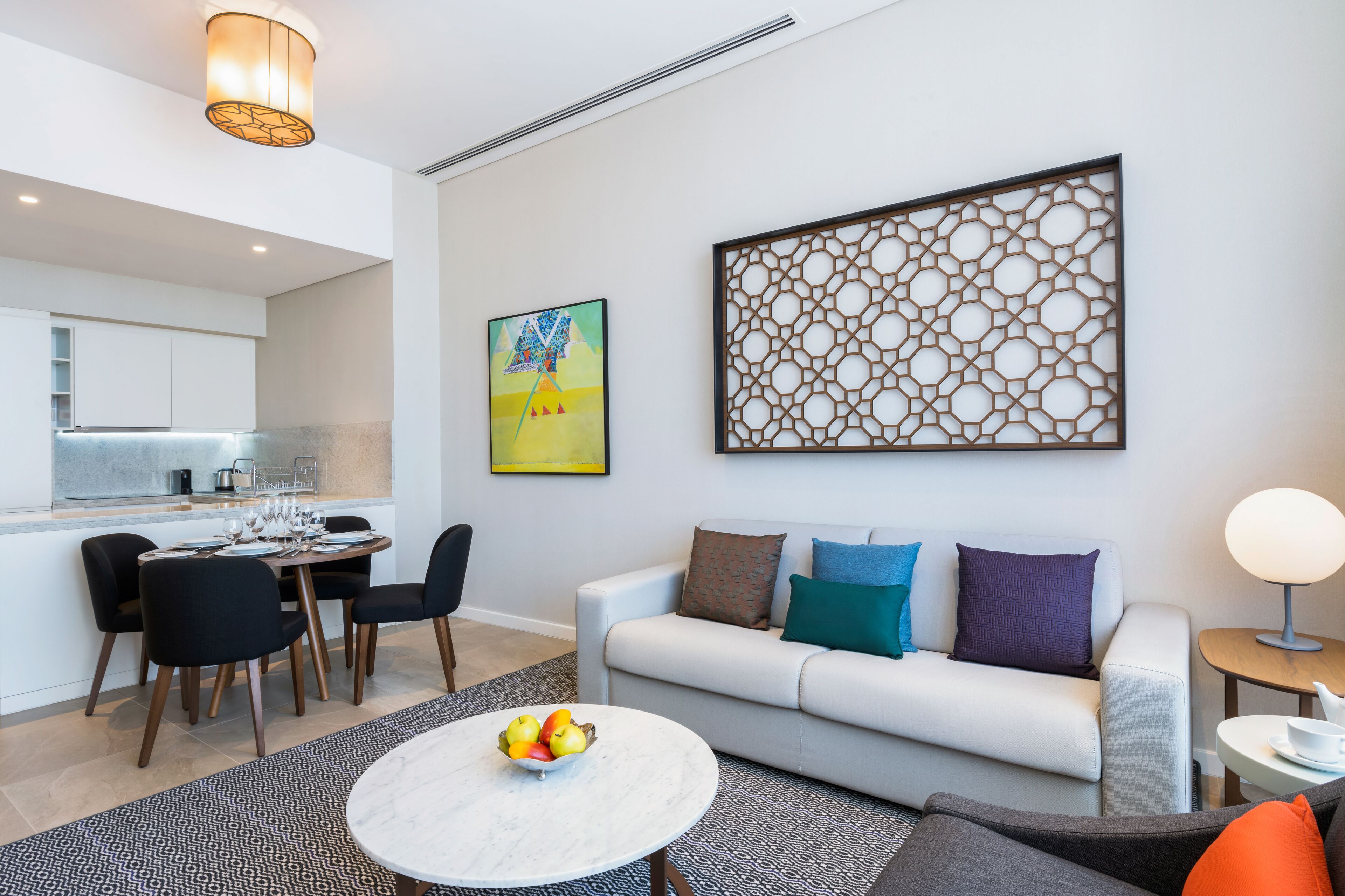 A modern living room with a white sofa, a dining area with a table set for four, and a kitchen in the background.