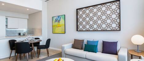 A modern living room with a white sofa, a dining area with a table set for four, and a kitchen in the background.