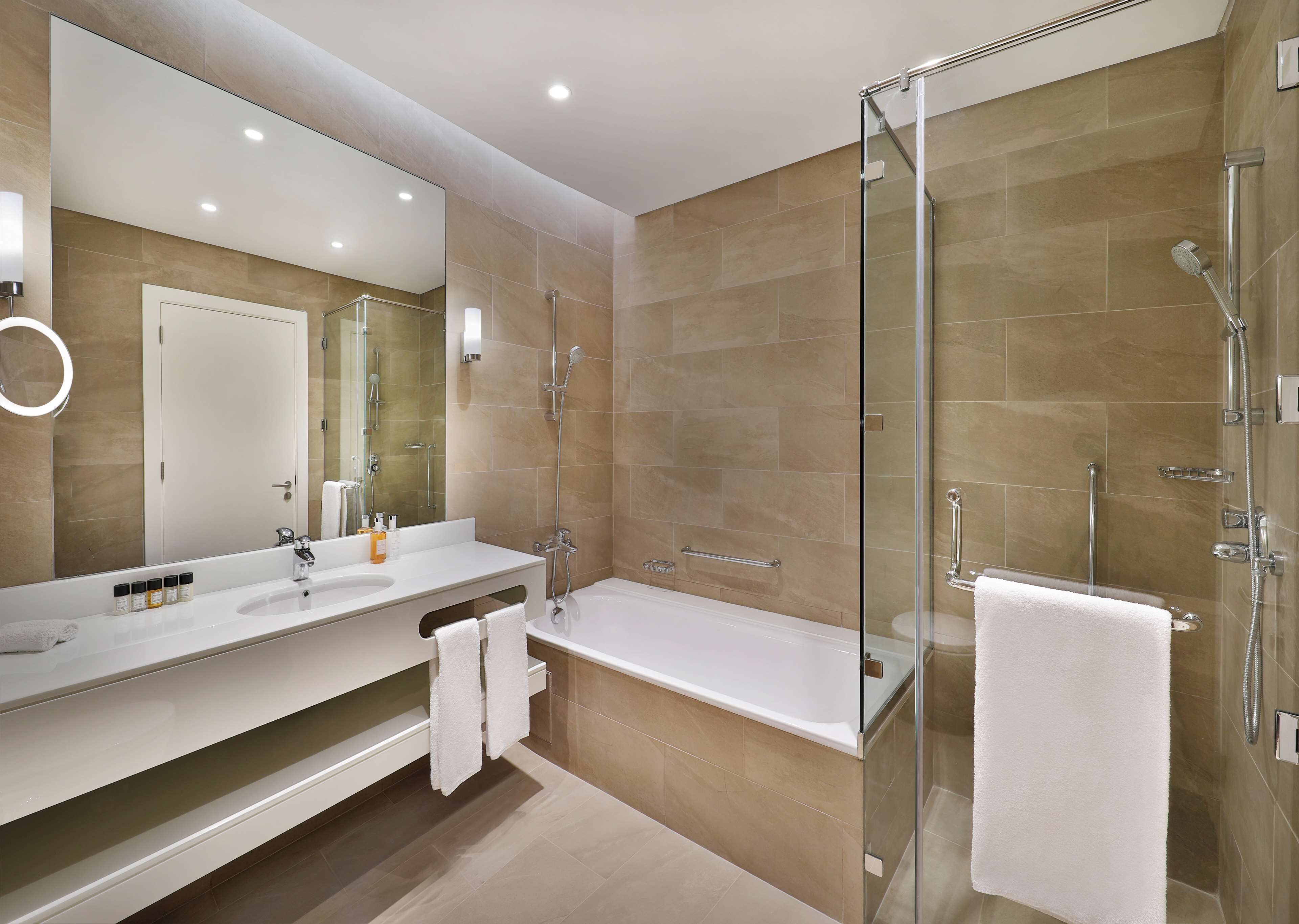 A modern bathroom with a glass-enclosed shower, a large mirror, and a white bathtub.
