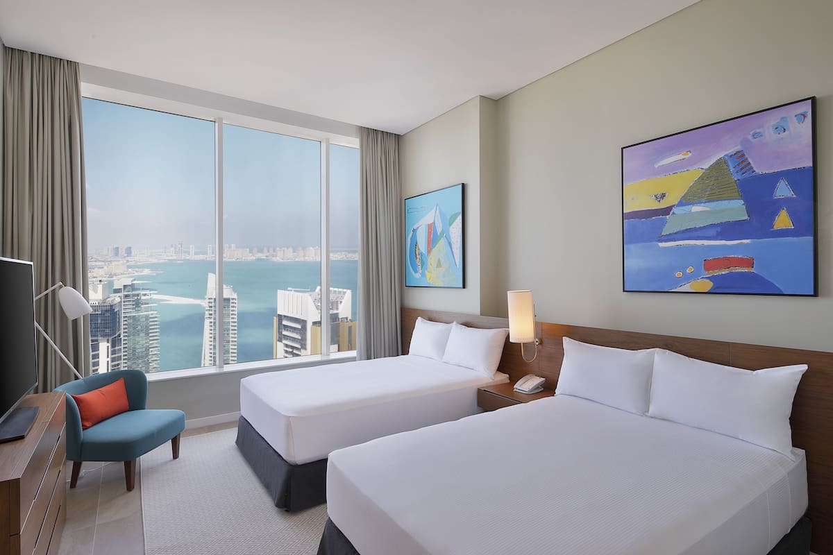 Habitació d'hotel amb dos llits, escriptori, cadira i una finestra gran que ofereix vista a la ciutat.
