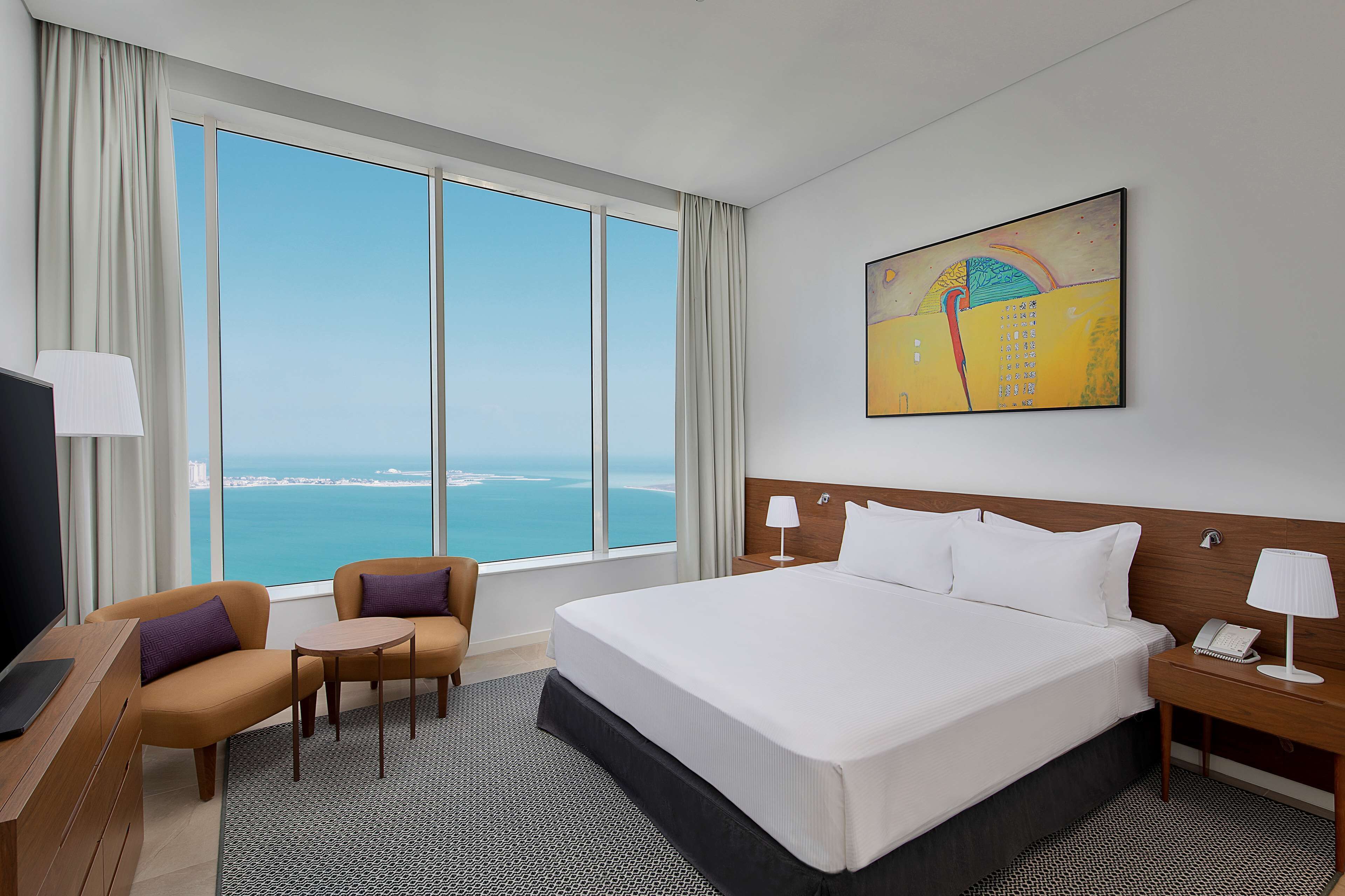 Une chambre d’hôtel avec un grand lit, un bureau avec une chaise, une télévision et une vue sur la mer.