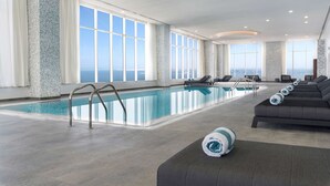 Una amplia piscina interior con vistas despejadas al océano, un área de descanso con sofás y un bar junto a la piscina.