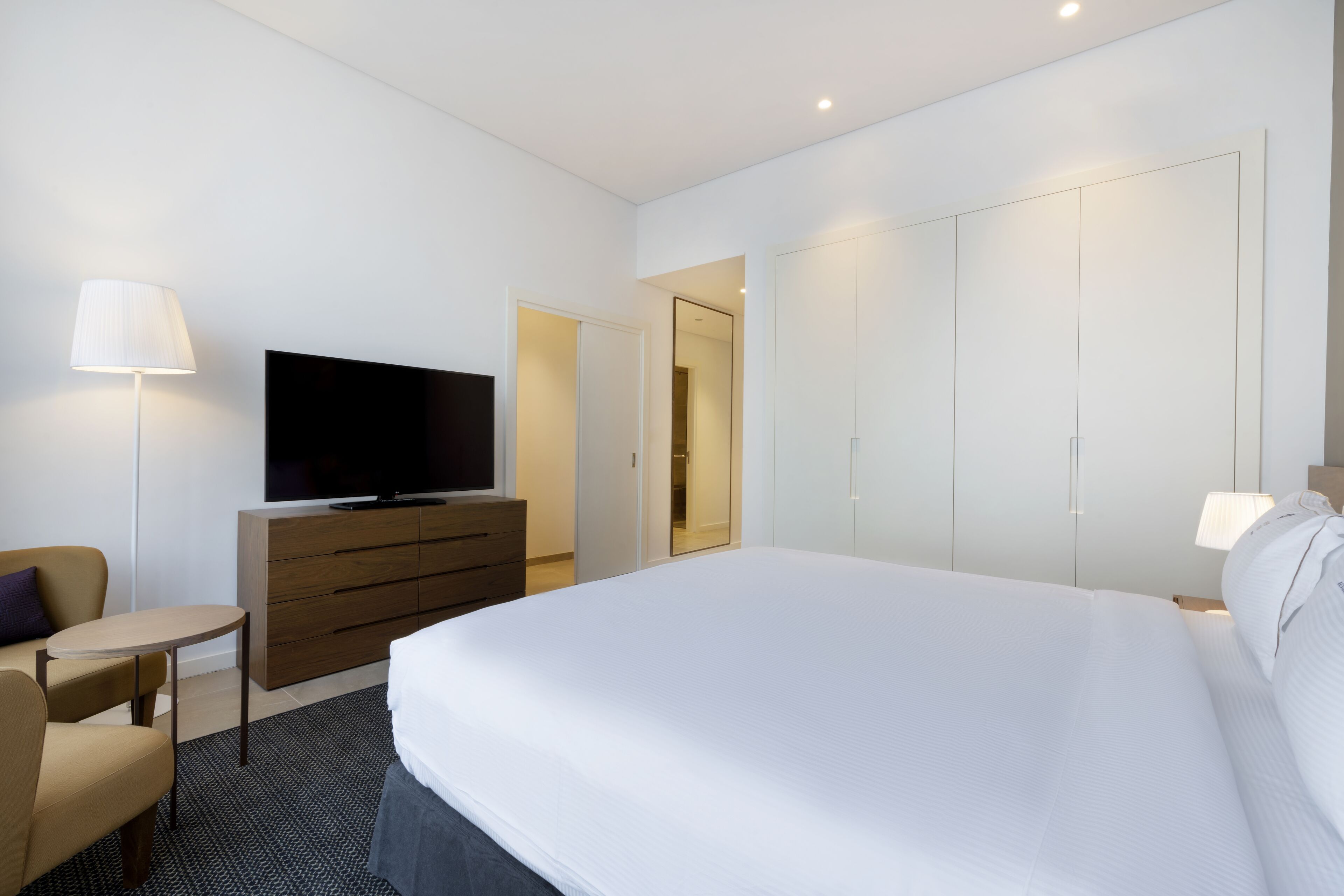 A hotel room with a large bed, a TV on a wooden dresser, a small table, a sofa, and a wardrobe.
