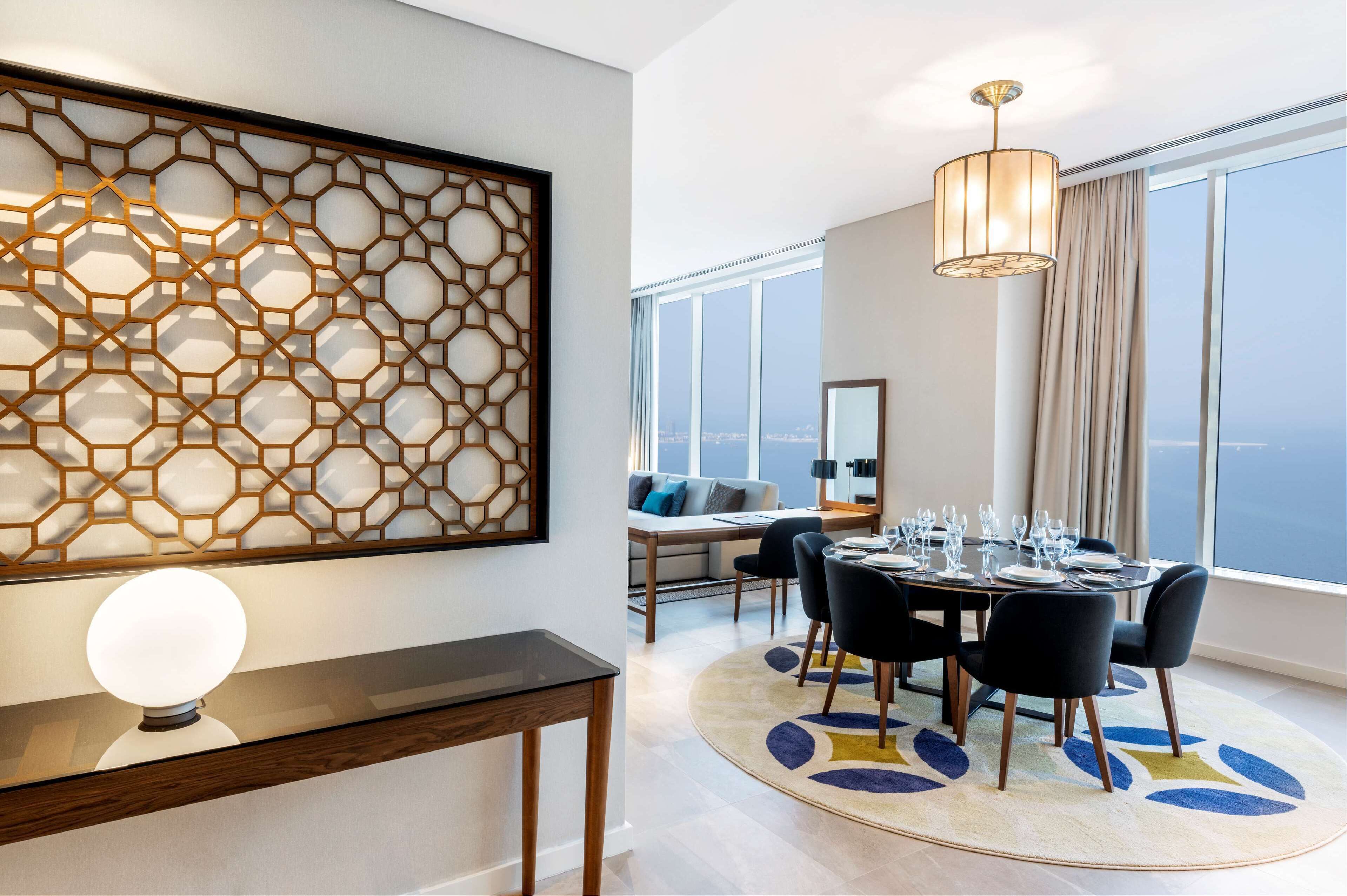 Un comedor moderno con una mesa redonda dispuesta para seis personas, un panel decorativo en la pared y un amplio ventanal con vistas.