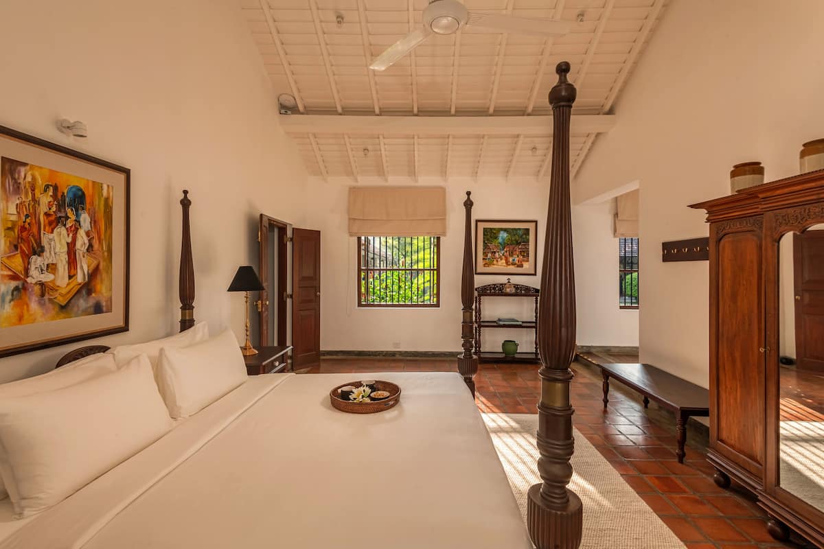 Um quarto espaçoso com uma cama grande, uma cama de dossel de madeira, um banco e uma estante com objetos decorativos.