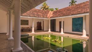 Una piscina con lirios acuáticos, un espacio cubierto con columnas y un tejado de baldosas.