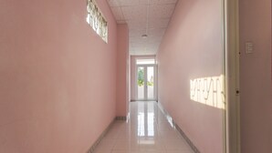 A long, narrow hallway with pink walls and a tiled floor, leading to a door at the end. - OYO 962 Tulip Motel (Da Nang)