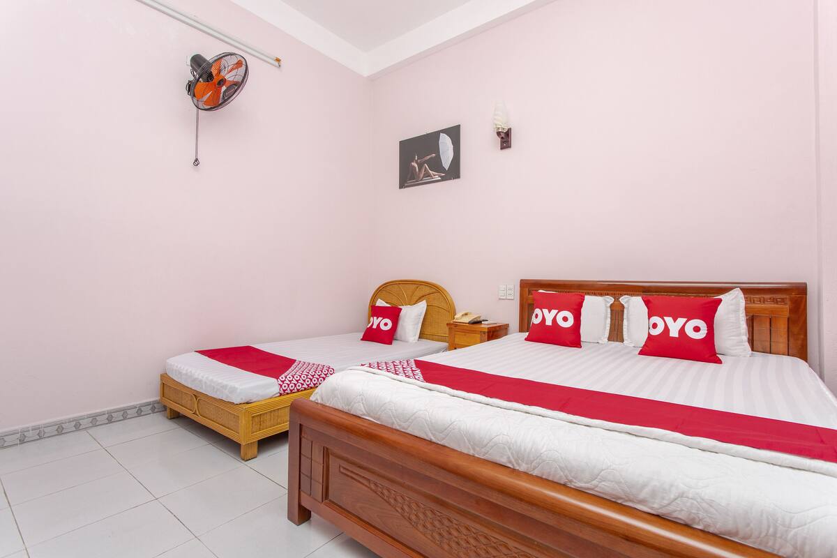 Habitación de hotel con dos camas, cada una con ropa de cama y almohadas rojas y blancas, una mesita pequeña y un ventilador de pared.