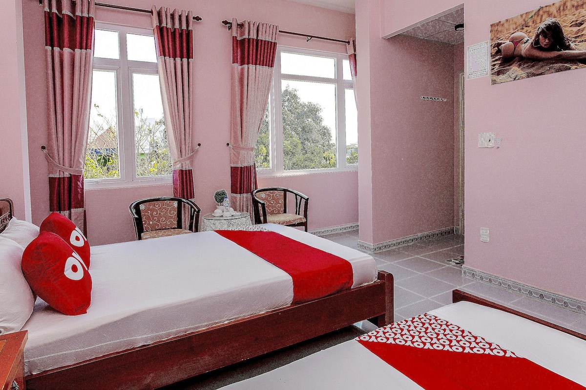 Una habitación con una cama, una silla, una mesita y un ventanal con cortinas.