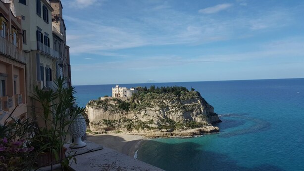 Un edificio costero con estructura similar a un castillo, ubicado en un acantilado y con vistas a la playa y al mar.