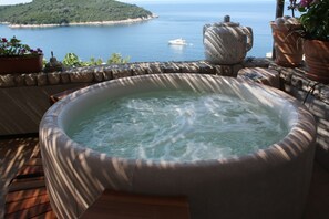 A hot tub on a wooden deck with a view of a body of water and a boat.