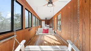 A wooden interior with a swing seat, ceiling fan, and large windows. - Ozarks Oasis 4 Bedroom Cabin by RedAwning (Branson)