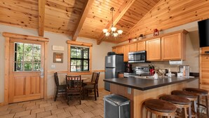 A wooden cabin kitchen with a dining area, a refrigerator, a microwave, and bar stools. - Ozarks Oasis 4 Bedroom Cabin by RedAwning (Branson)