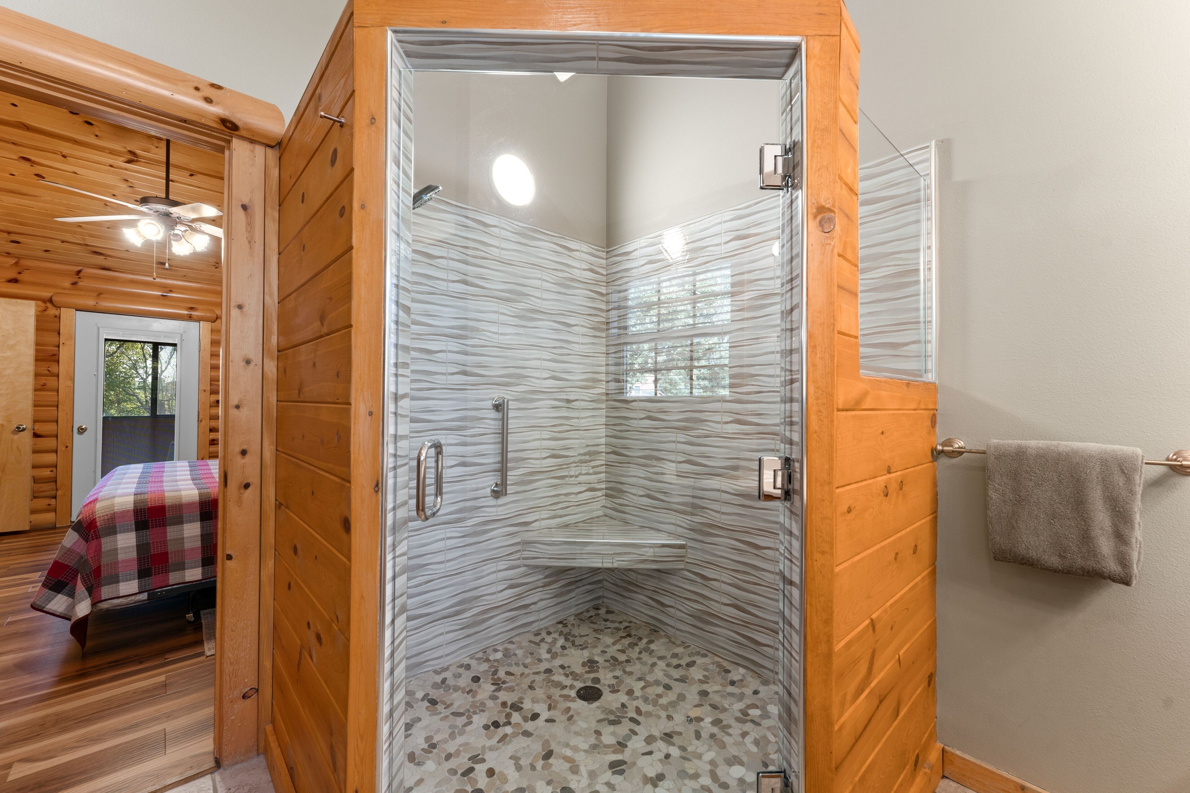 A corner shower with a pebble floor, wooden walls, and a glass door.