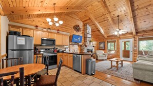 A spacious kitchen with wooden cabinets, a refrigerator, a microwave, and a dining area with a table and chairs. - Ozarks Oasis 4 Bedroom Cabin by RedAwning (Branson)