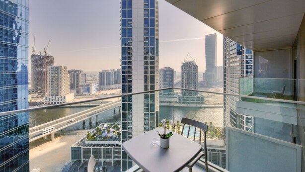 Un balcone con tavolo e sedia, affaccio su una vista urbana che include grattacieli e un fiume.