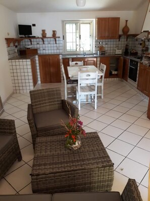 Een woonkamer met een bank en salontafel, een eethoek met tafel en stoelen, en een keuken met houten kastjes en een betegelde spatwand.