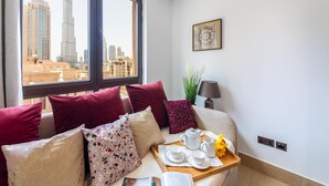 A hotel room with a city view, a bed with red and patterned pillows, a bedside table with a tray of tea and a lamp. - Maison Privee - Luxury Living Next to Dubai Mall & Burj Khalifa (Dubai)