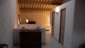 Un couloir étroit avec un plafond en bois, une petite table sur laquelle se trouve un vase, et une porte sur le côté droit.