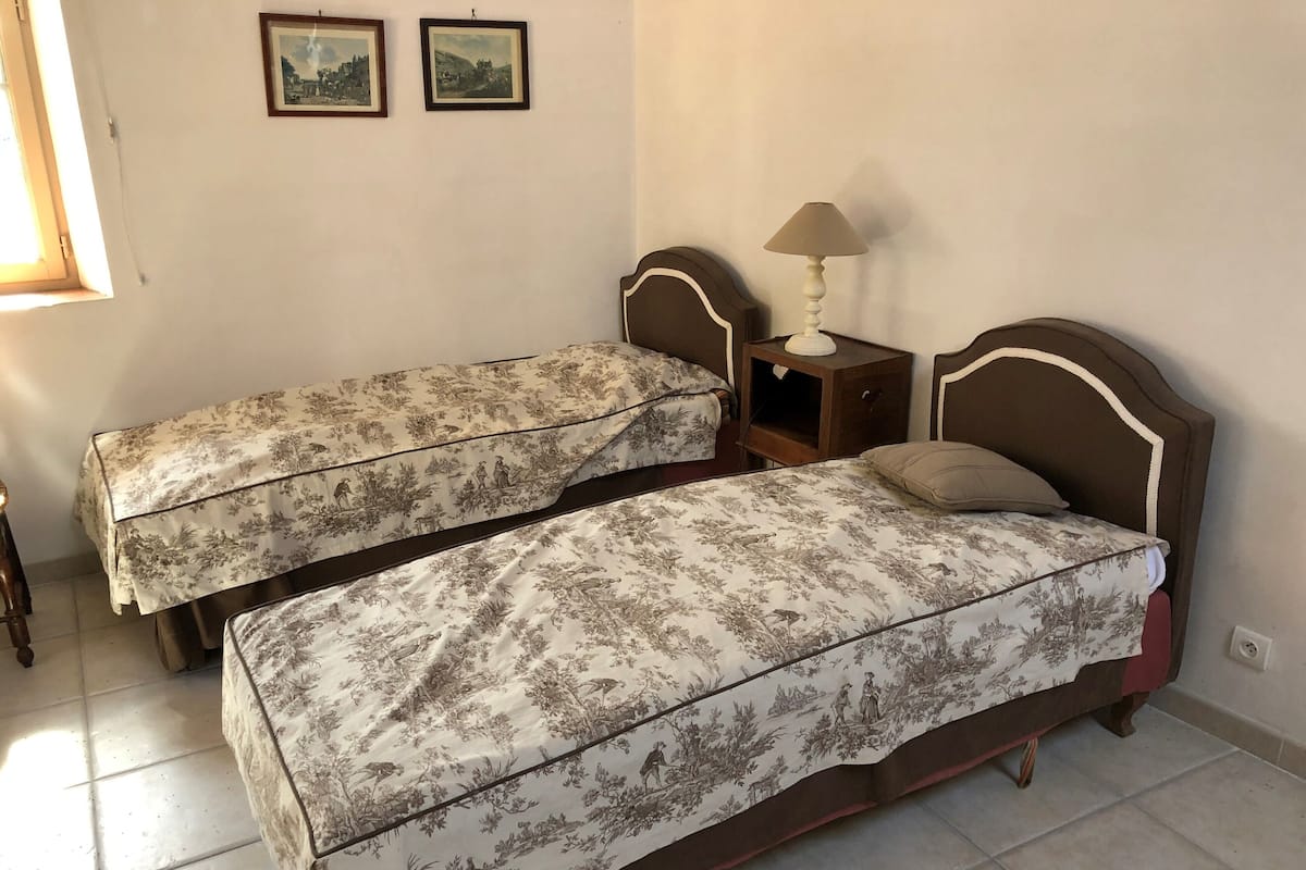 A bedroom with two single beds, a nightstand with a lamp, and two framed pictures on the wall.