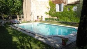 Une piscine entourée d’un mur de pierre, avec un bâtiment en arrière-plan.