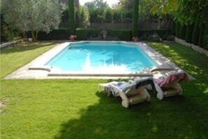 Uma piscina retangular com borda azulejada, rodeada por um relvado bem cuidado e um sebedal.