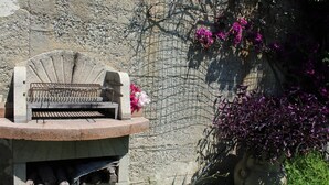 A stone bench with a metal grill, a concrete planter with flowers, and a wire fence against a stone wall. - Villa Faro with fragrant garden and unforgettable panoramic view! 350m (RICADI)