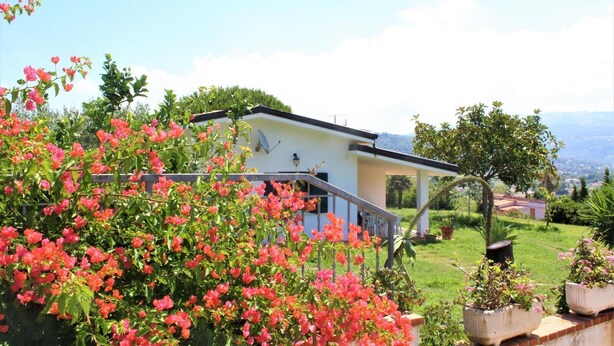 A house with a balcony, surrounded by lush greenery and flowering plants. - Villa Faro with fragrant garden and unforgettable panoramic view! 350m (RICADI)