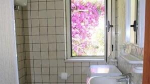 A bathroom with a toilet, bidet, sink, and a window with a view of pink flowers. - Villa Faro with fragrant garden and unforgettable panoramic view! 350m (RICADI)