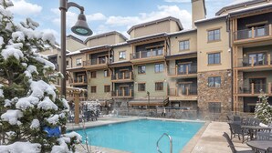 A multi-story hotel with a pool area, featuring balconies and a mix of stone and wood exteriors.
