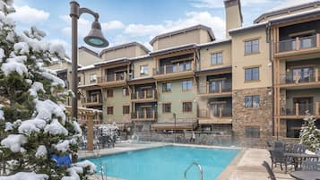 Un hotel de varios pisos con área de piscina, que cuenta con balcones y una combinación de fachada de piedra y madera.