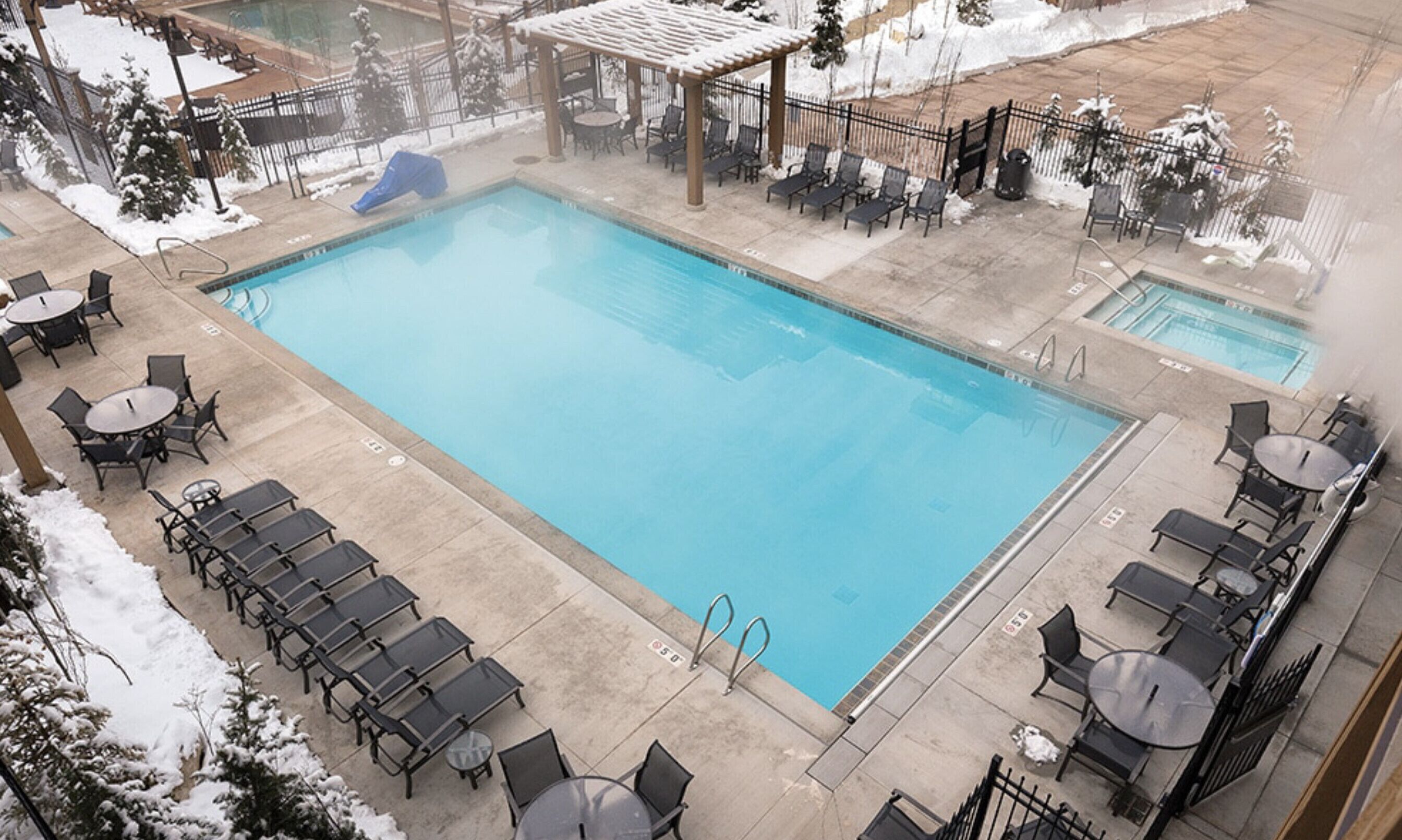 A rectangular pool with a blue water feature, surrounded by lounge chairs and tables.