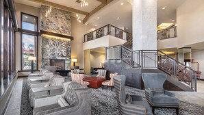A spacious lobby with a stone fireplace, multiple seating areas, and a staircase leading to an upper level.