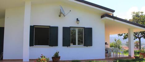 A white building with two windows and a satellite dish. There are potted plants in front of the building.