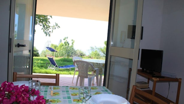 Un comedor con una mesa dispuesta para dos, un televisor sobre un mueble y vistas al jardín.