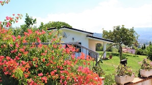 Una casa con balcón, rodeada de abundante vegetación y plantas florecientes.