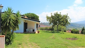 Una casa con porche cubierto, césped y vista al campo.