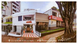 A hostel with a checkered entrance, a restaurant named 'Presto' across the street, and a tree in the foreground. - Nogal Hostel (Pereira)