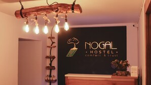 A reception desk with a sign reading "NOGAL HOSTEL comfort & trust" and a wooden wall decor with hanging light bulbs. - Nogal Hostel (Pereira)
